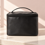 Soft Spell black PU beauty bag on a light vanity countertop in natural sunlight.